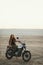 Young beautiful woman sitting on her old cafe racer motorcycle in desert at sunset or sunrise