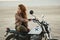 Young beautiful woman sitting on her old cafe racer motorcycle in desert at sunset or sunrise