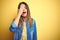 Young beautiful woman standing over yellow isolated background Yawning tired covering half face, eye and mouth with hand