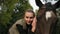 Young beautiful woman stroking brown horse while sitting in the saddle and putting her head on the horse`s head looking