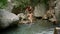 Young beautiful woman swinging on a wooden swing hanging by rope on a tree branch over river in woods with rocks in