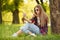 Young beautiful woman takes selfie on cell phone sitting on grass in summer city park. Blow kiss. Beautiful modern girl in