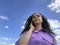 Young beautiful woman talking on mobile phone, standing under blue sky with white clouds. Cute vivid female with