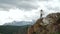 Young beautiful woman traveler wearing hat and poncho relaxing on the top of the hill with mountains and hills around