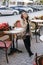 Young beautiful woman in trench coat drinking coffee in a street cafe