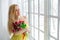 Young beautiful woman with tulip bunch in yellow dress looks at window.