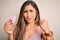 Young beautiful woman using beauty sponge with facial makeup over pink background annoyed and frustrated shouting with anger,