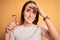 Young beautiful woman using eyelash curler standing over isolated yellow background stressed with hand on head, shocked with shame