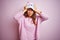 Young beautiful woman wearing funny cat cap standing over pink isolated background suffering from headache desperate and stressed