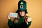 Young beautiful woman wearing green hat and glasses on saint patricks day celebration pointing with finger to the camera and to