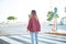 Young beautiful woman wearing red jacket walking over crosswalk on backview at the town street