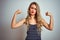 Young beautiful woman wearing stripes t-shirt standing over white isolated background showing arms muscles smiling proud