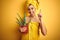 Young beautiful woman wearing a towel holding cactus pot over yellow  background surprised with an idea or question