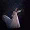 Young beautiful woman in wedding dress with wide light skirt. Dark background, fantasy style.