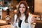 Young beautiful woman in white blouse looks hungry holding fresh meat burger in one hand and fries in another during lunch in cafe