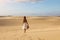 Young beautiful woman with white dress walking in the desert dunes  during sunset. Girl walking on golden sand on Corralejo Dunas