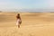 Young beautiful woman with white dress walking in the desert dunes  during sunset. Girl walking on golden sand on Corralejo Dunas