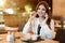 Young beautiful woman in white stylish blouse looks hungry eating meat burger with fries for lunch in trendy cafe while having