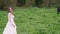 A young beautiful woman in a white wedding dress stands in a field with horses.