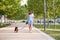 Young beautiful young brunette cheerful girl in blue dress walks with her dog in a city park. Dog breed Pharaoh on leash