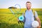 A young beauty man on picnic with backpack, rackets for badbotton and ball smiles against background of a green meadow