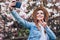 Young beauty woman in summer hat take selfie on phone near blossom magnolia tree in sunny spring day