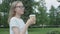 Young bespectacled young woman drinking a cup of coffee in park on summer day calmly and confidently looking away from