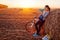 Young bicyclist having rest after a ride in autumn field at sunset. Woman drinking water by haystack and using phone