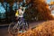 Young bicyclist having rest after a ride in autumn field at sunset. Woman drinking water on road