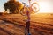 Young bicyclist raising her bicycle in autumn field. Happy woman celebrates victory holding bike in hands