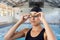 Young biracial female swimmer adjusting goggles at an indoor pool