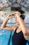 Young biracial female swimmer adjusting goggles at poolside indoors