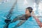 Young biracial female swimmer resting at pool edge indoors, wearing goggles