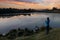 Young birdwatcher woman standing with binoculars near the pond in the evening