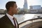 Young black businessman wearing shirt and tie standing by the River Thames, London, looking away, backlit