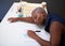 A young Black businesswoman falls asleep while reading reports at her desk