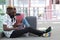 Young black couple buying their travel tickets on a laptop, sitting at the station with their suitcases