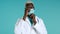 Young black doctor puts on face medical mask during coronavirus pandemic. Medical stuff portrait on blue background