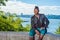 A young black guy with mohawk hair is sitting on a rocky stone by a river, relaxing