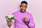 Young black man holding bouquet of flowers and wedding ring smiling and laughing hard out loud because funny crazy joke