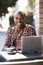 Young black man with laptop outside a cafe looking to camera