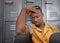 A young black man sits, head in his hand on campus looking upset, stressed