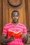 Young black man standing by office door in New York City, reading red book