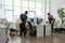 Young black man in workwear cleaning floor while girl wiping desks with computers