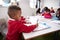 Young black schoolboy wearing school uniform sitting at a desk in an infant school classroom drawing, close up, side view