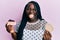 Young black woman with braids eating cake slice and rice crackers sticking tongue out happy with funny expression