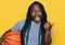 Young black woman with braids holding basketball ball pointing thumb up to the side smiling happy with open mouth