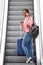 Young black woman on escalator with mobile phone and suitcase