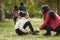 Young black woman helping her daughter to tie her shoes during a family walk in the park, low angle