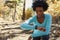 Young black woman kneeling in a forest checking smartwatch